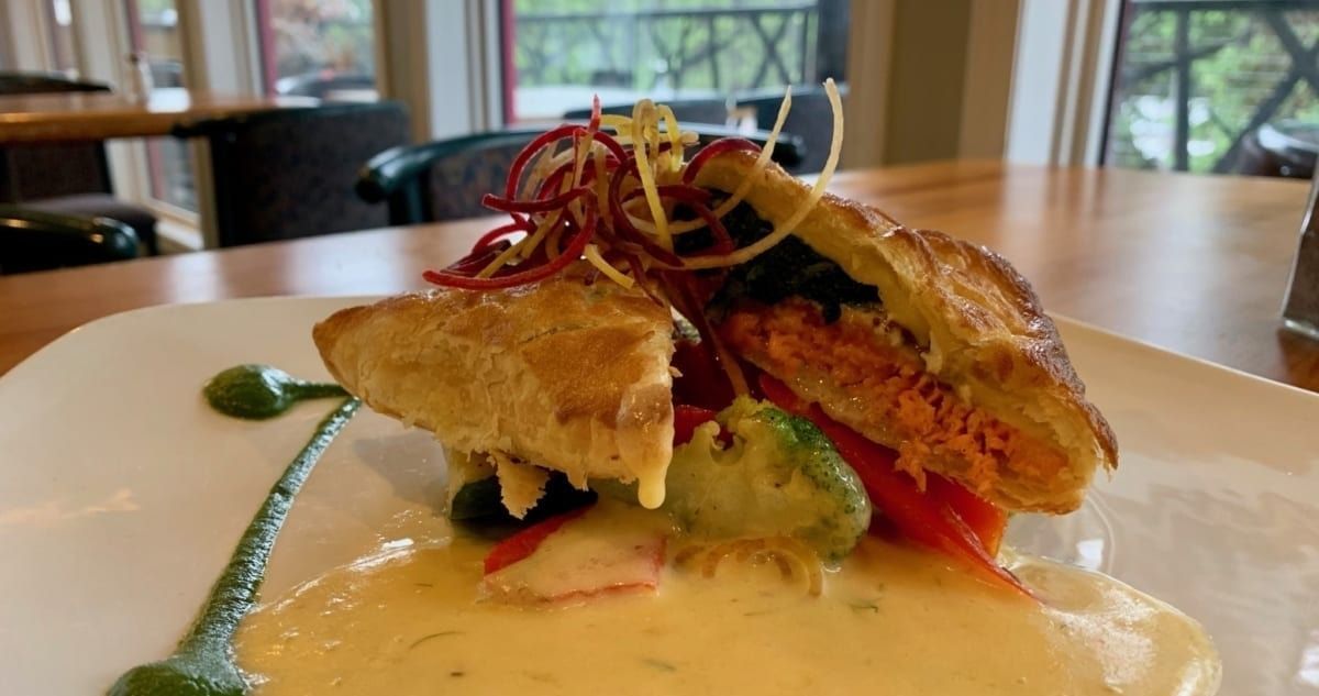 Gourmet dish on white plate with sauce, vegetables, and pastry.