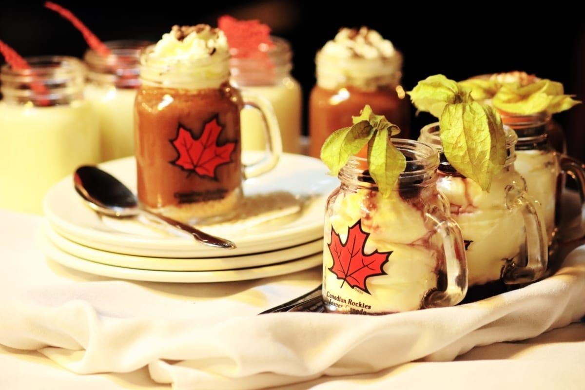 Desserts in small jars, some with whipped cream, maple leaf logo on jars, served on a tray.