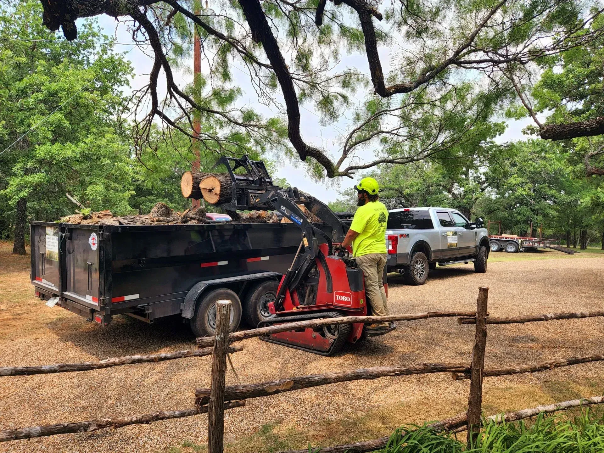 A man is standing next to a trailer filled with logs.