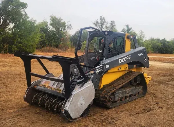 A yellow and gray tractor is sitting in a dirt field.