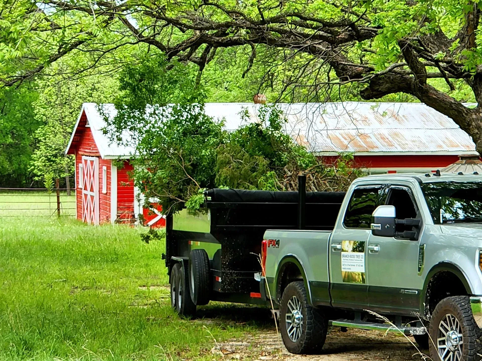 A truck with a trailer attached to it is parked in front of a red barn.