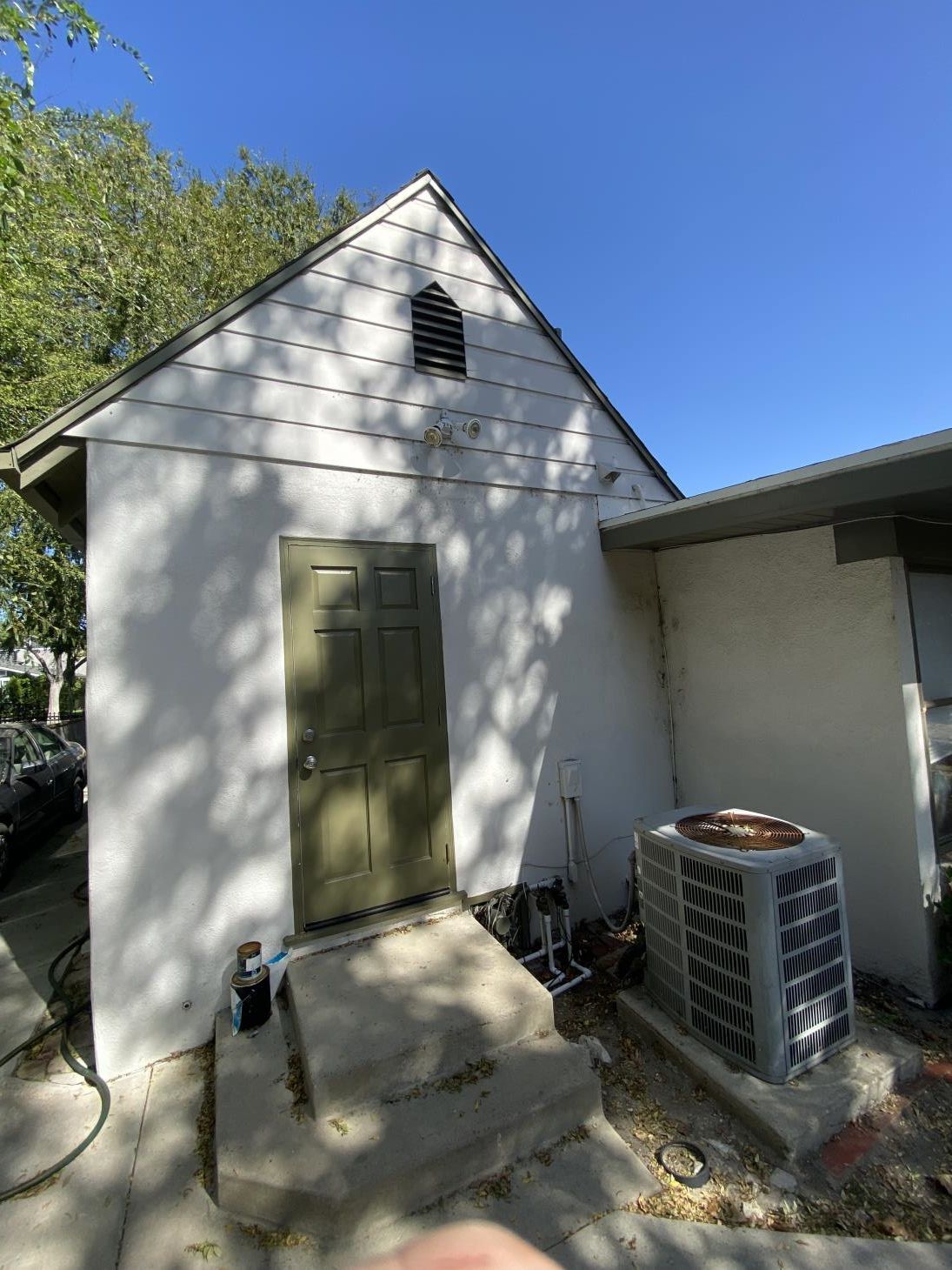 A white house with a green door and an air conditioner in the backyard.