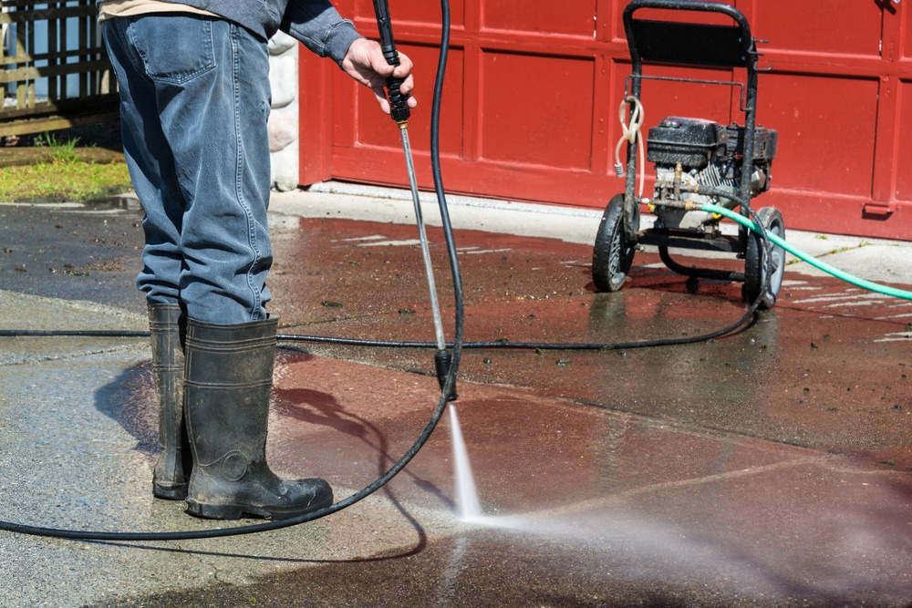 a man is using a high pressure washer to clean a driveway .