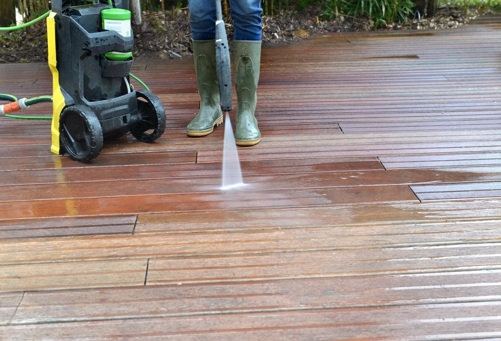 a person is using a high pressure washer to clean a wooden deck .