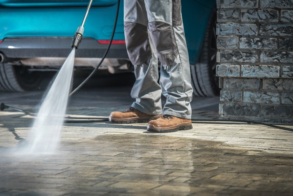 a man is using a high pressure washer to clean a driveway .