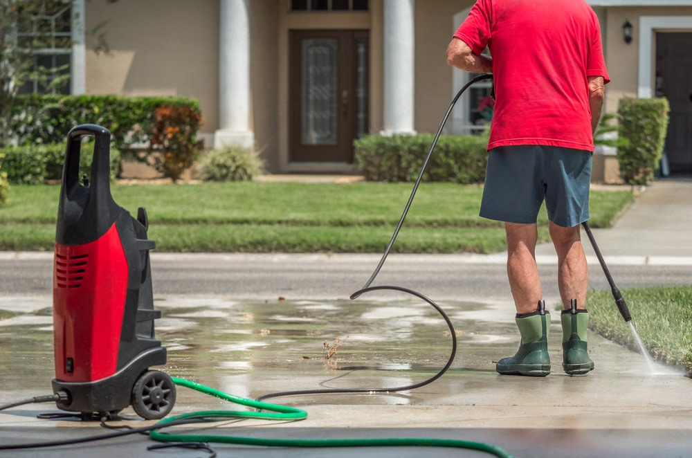 a man is using a high pressure washer to clean the driveway of a house .