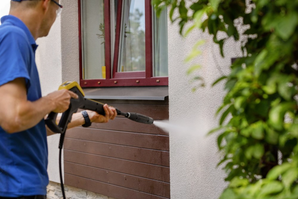 a man is using a high pressure washer to clean the side of a house .