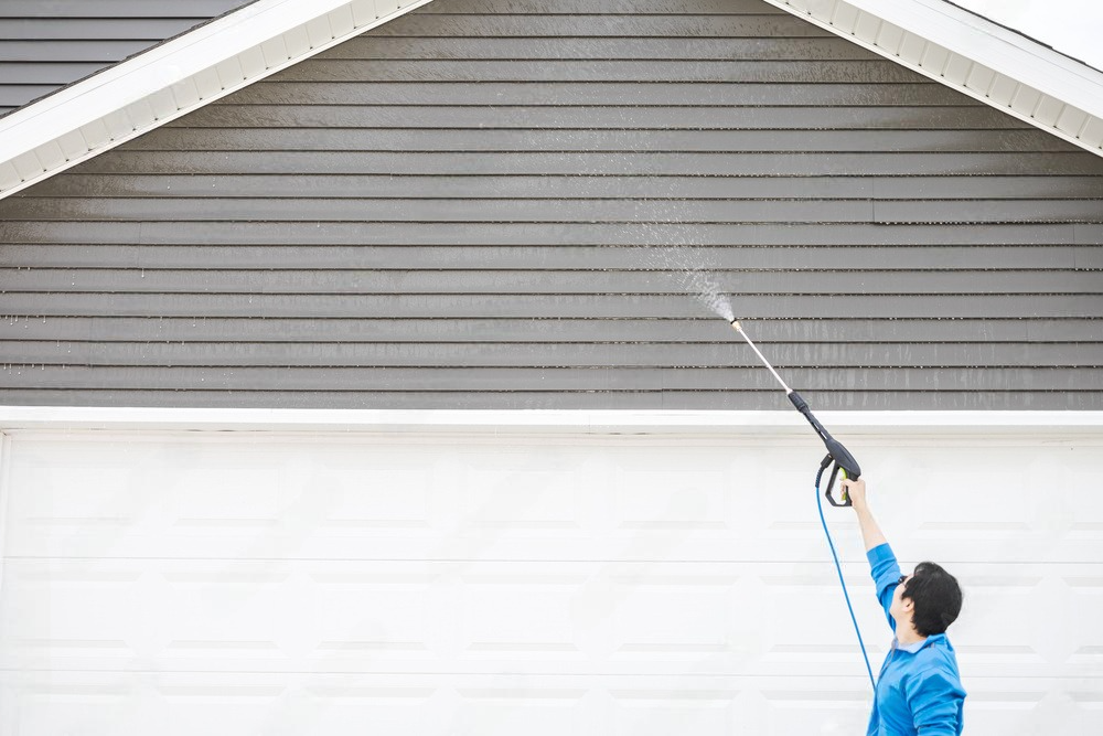 a man is using a high pressure washer to clean the side of a house .