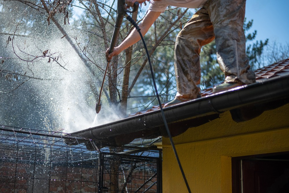 a man is cleaning the gutters of a house with a high pressure washer .