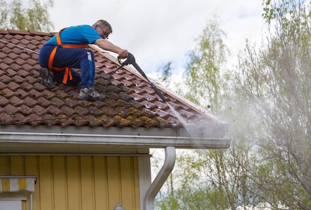 a man is cleaning the roof of a house with a high pressure washer .