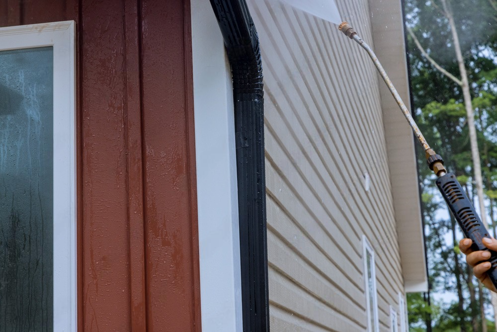 Man using a pressure washer to clean the exterior of the upper floor of a house, removing dirt and grime effectively.