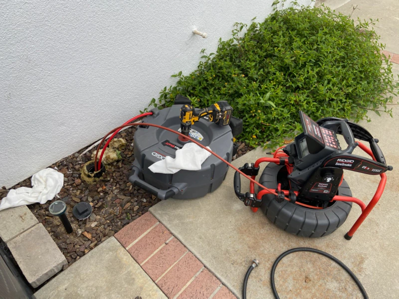 A drain camera is sitting on a sidewalk next to a hose