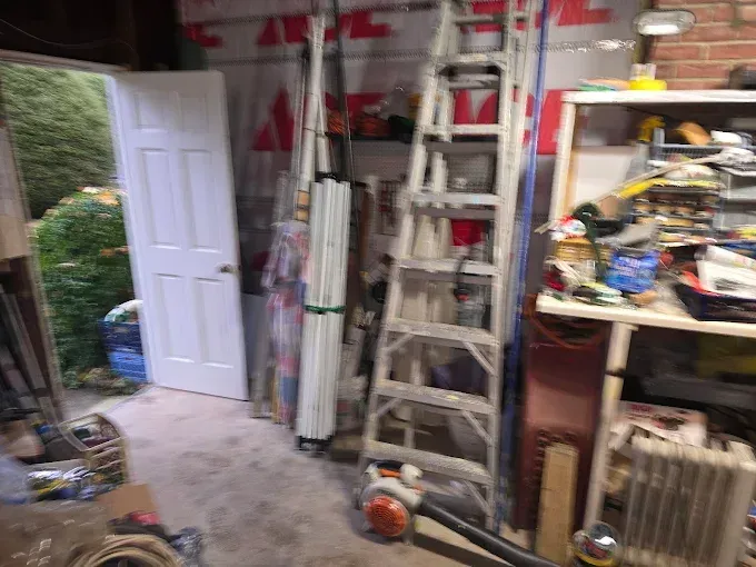 Garage interior with a ladder, door, and cluttered shelves.