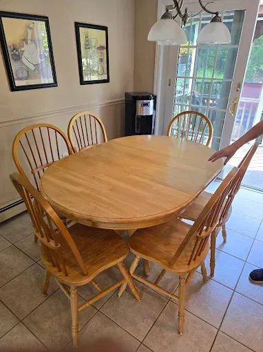 Dining table with six wooden chairs in a bright room, near a glass door and two framed pictures.