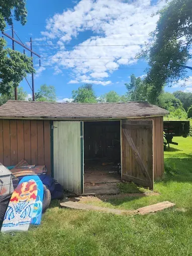 Wooden shed with open doors; a blue sky and trees in the background.