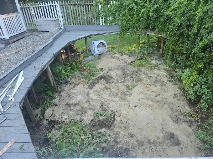 A deck overlooks a sandy patch with vegetation. An air conditioner sits in the middle.
