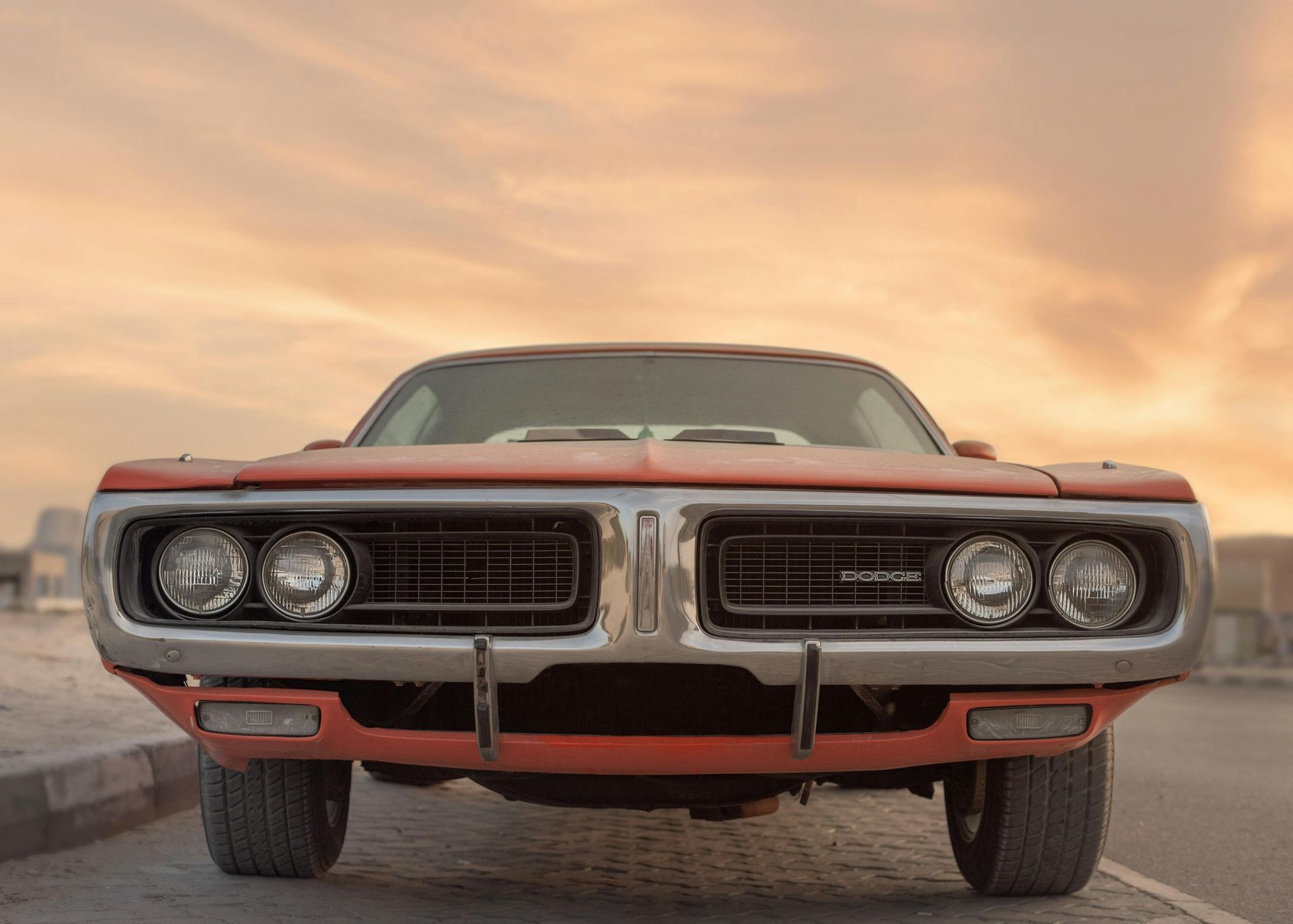 Classic red Dodge Charger, front view, sunset background.