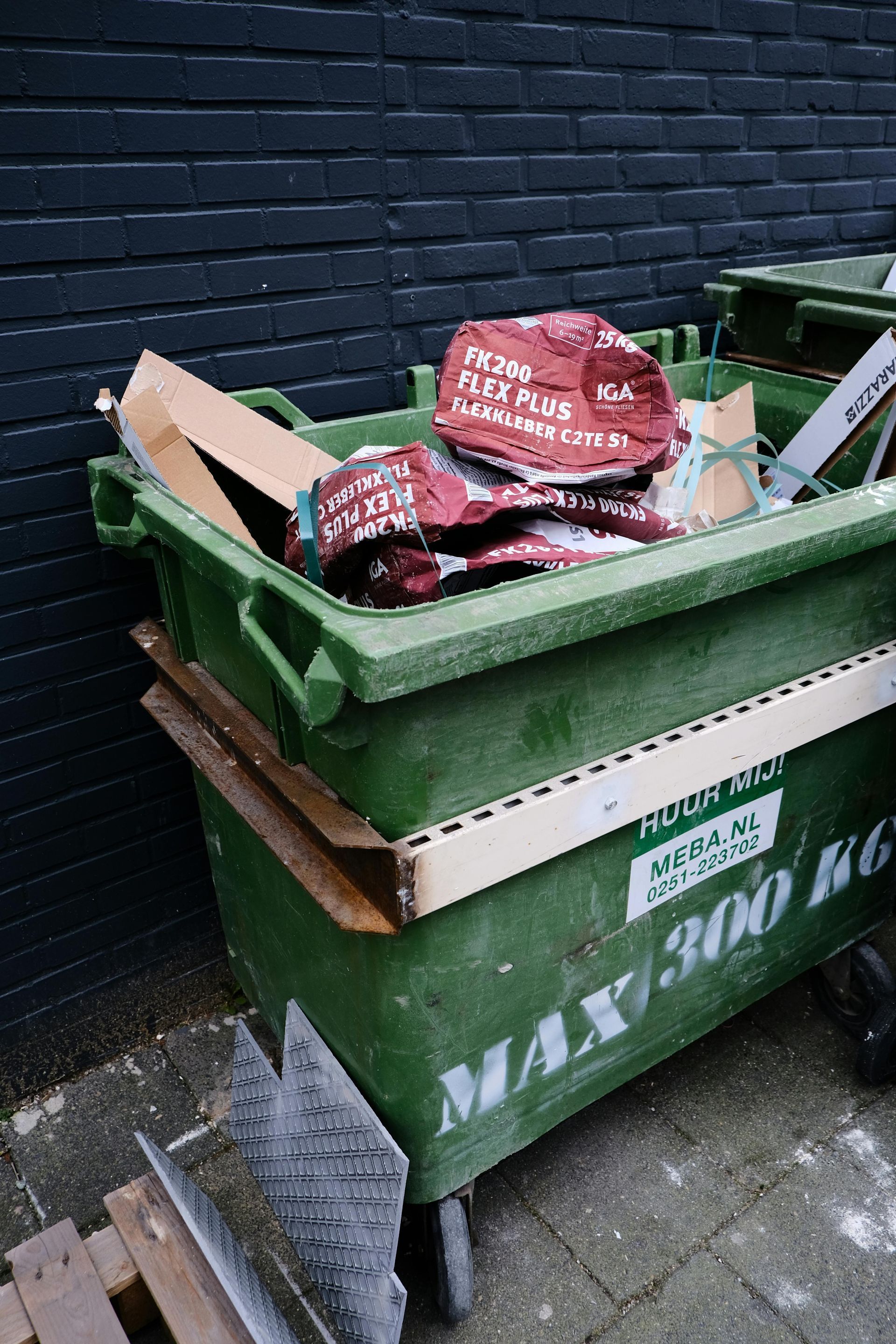 Green dumpster overflowing with debris; red bags and cardboard visible.