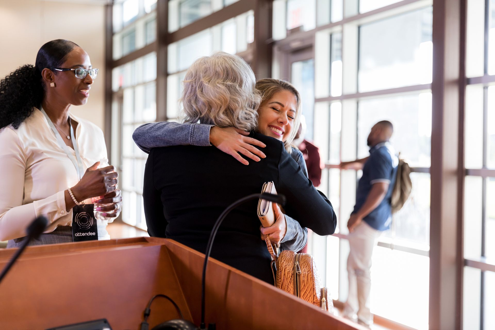 Excited woman hugs her female friend while attending a conference. Excited woman hugs her female friend while attending a conference.
