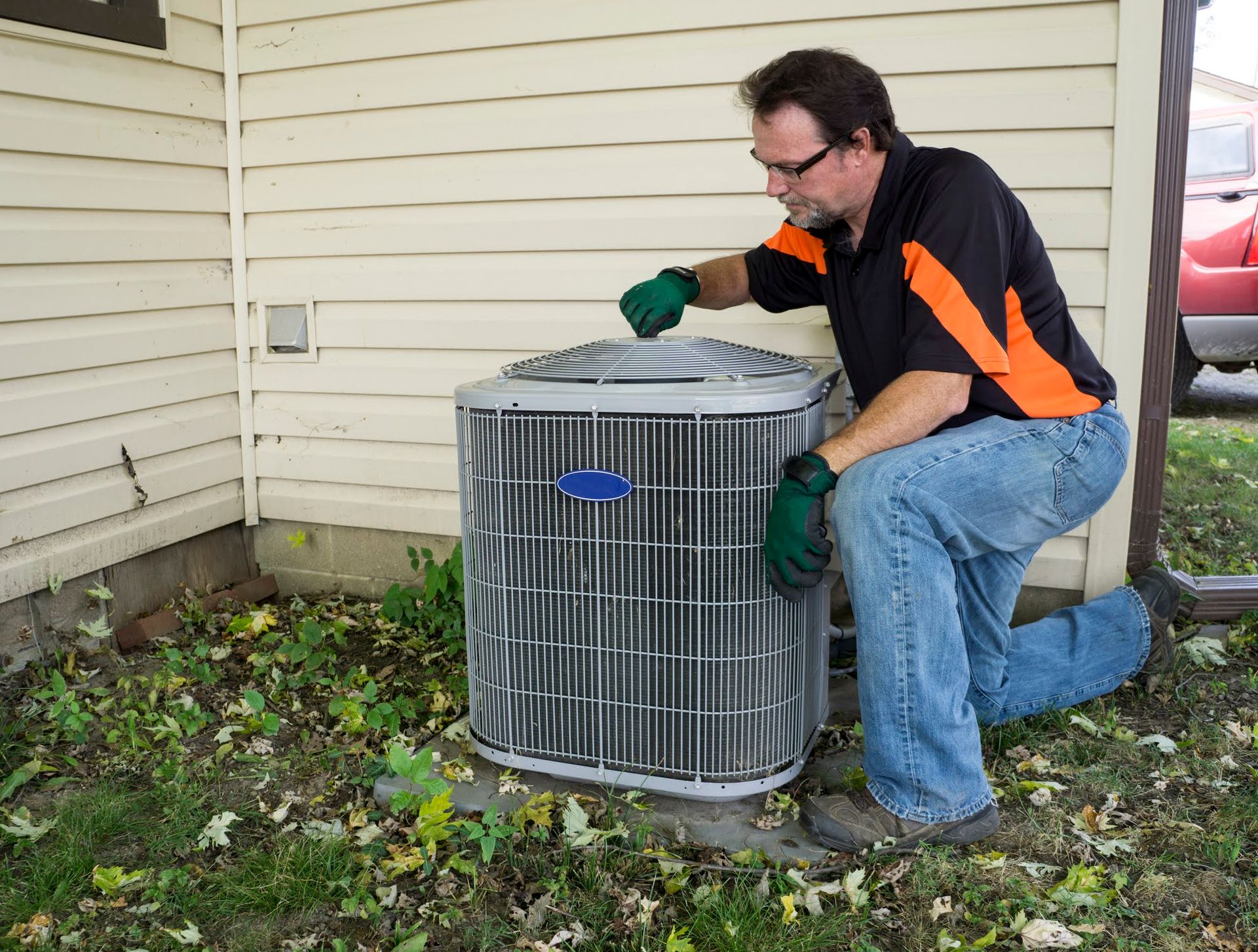 A man is working on an air conditioner outside of a house.