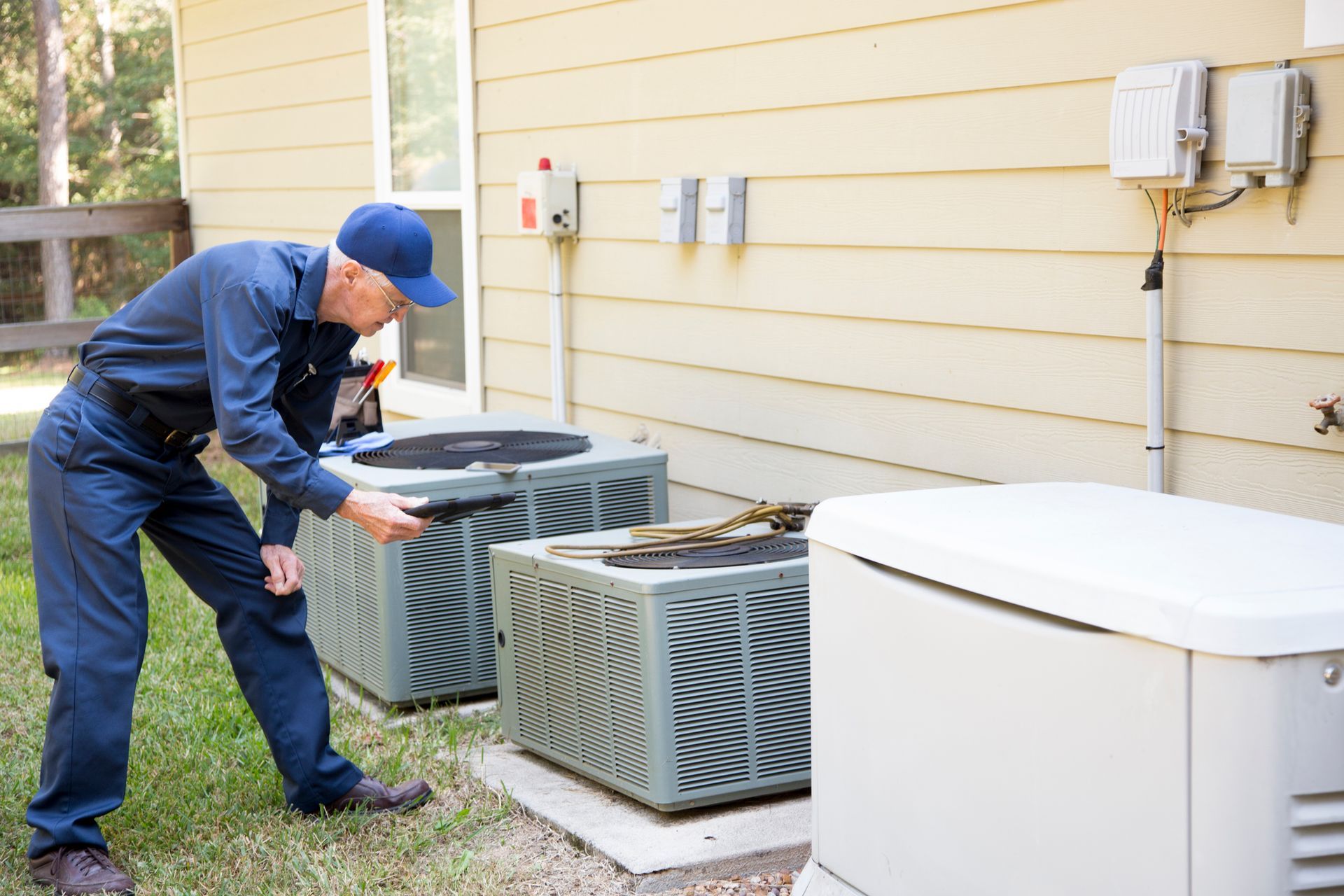 Technician services and checks on a pair of HVAC units and a gas generator on the side of a home.