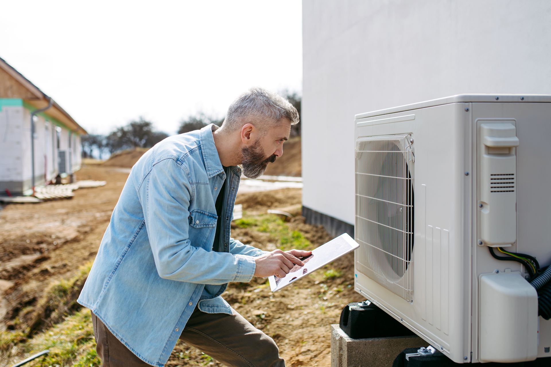 Technician inspecting outdoor unit during air conditioning installation on new residential property.