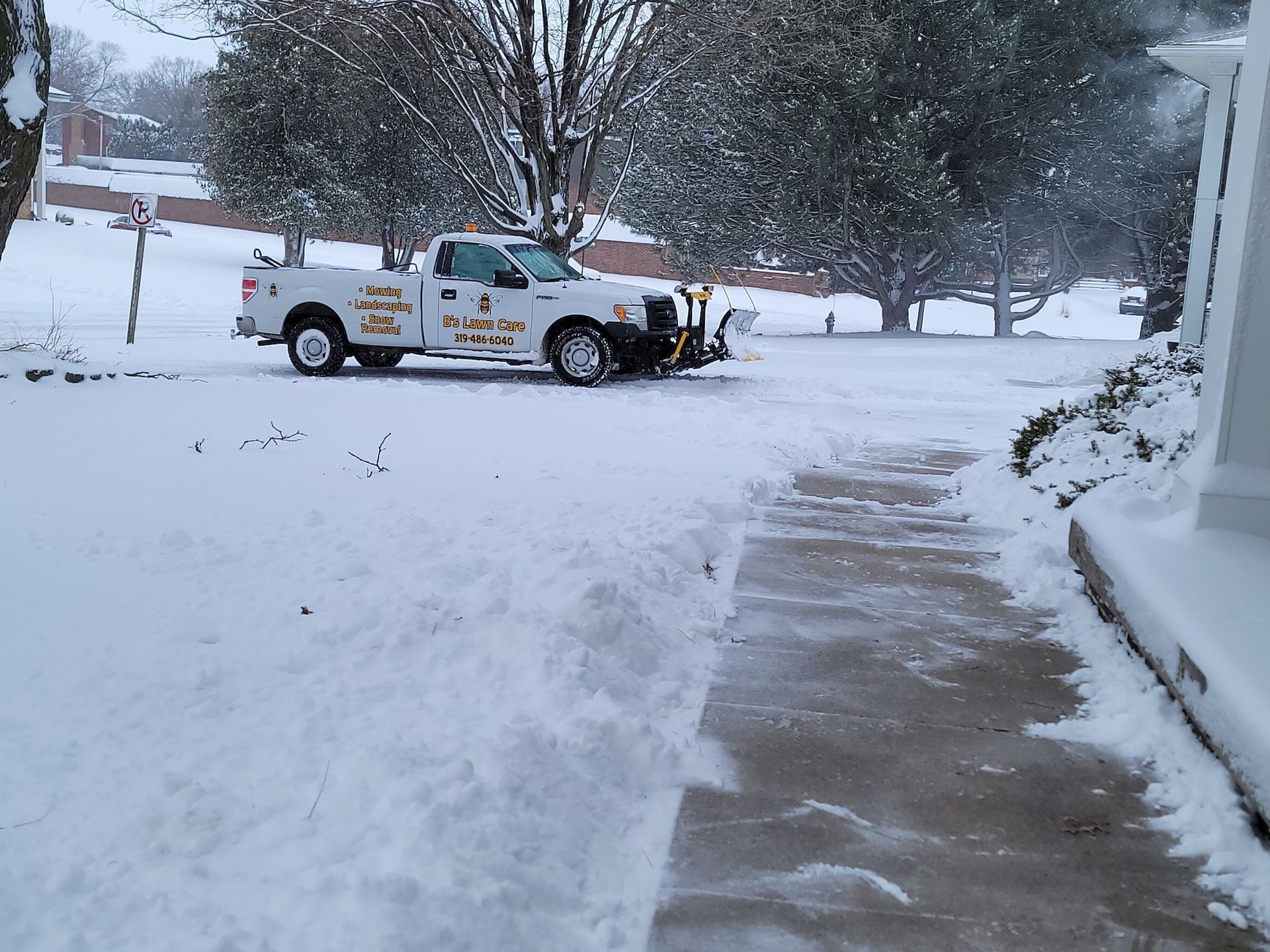 A white truck is parked in the snow next to a sidewalk.