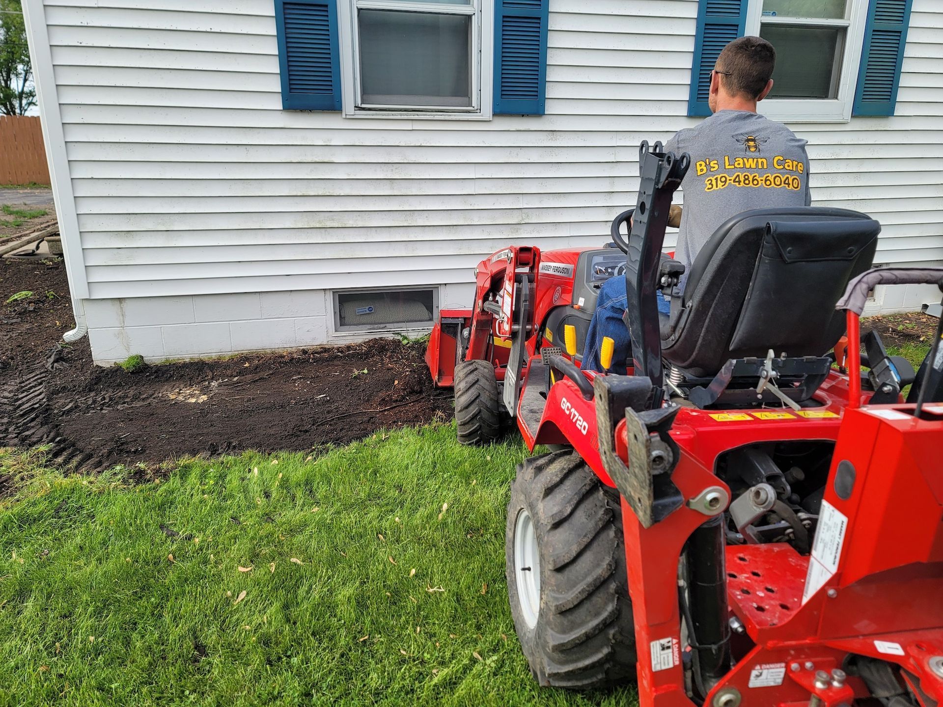 A man is driving a red tractor in front of a house.