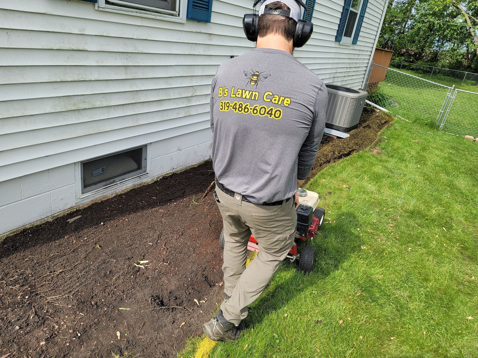 A man wearing headphones is standing next to a lawn mower in front of a house.