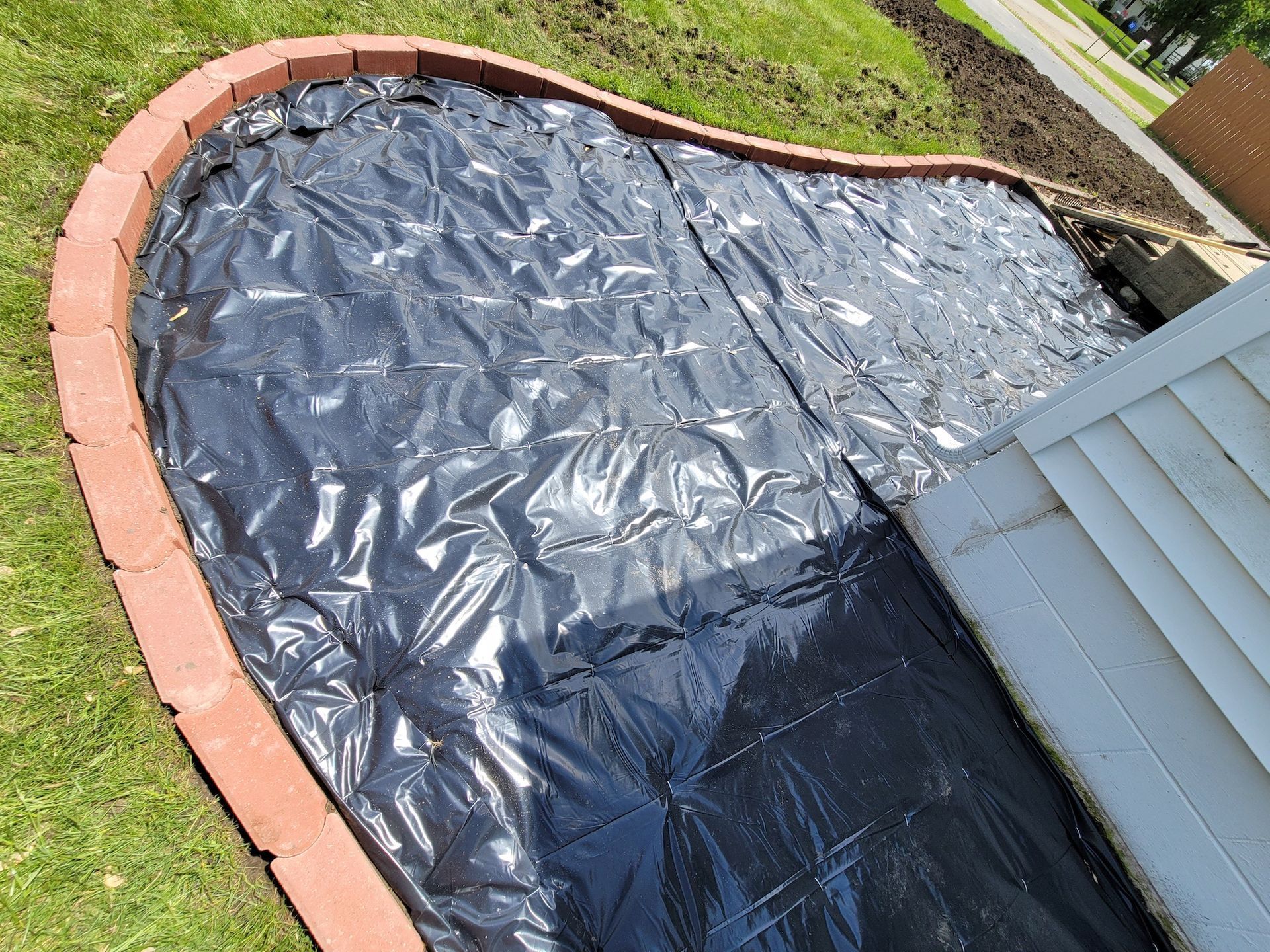 A black tarp is covering a brick border in a yard.