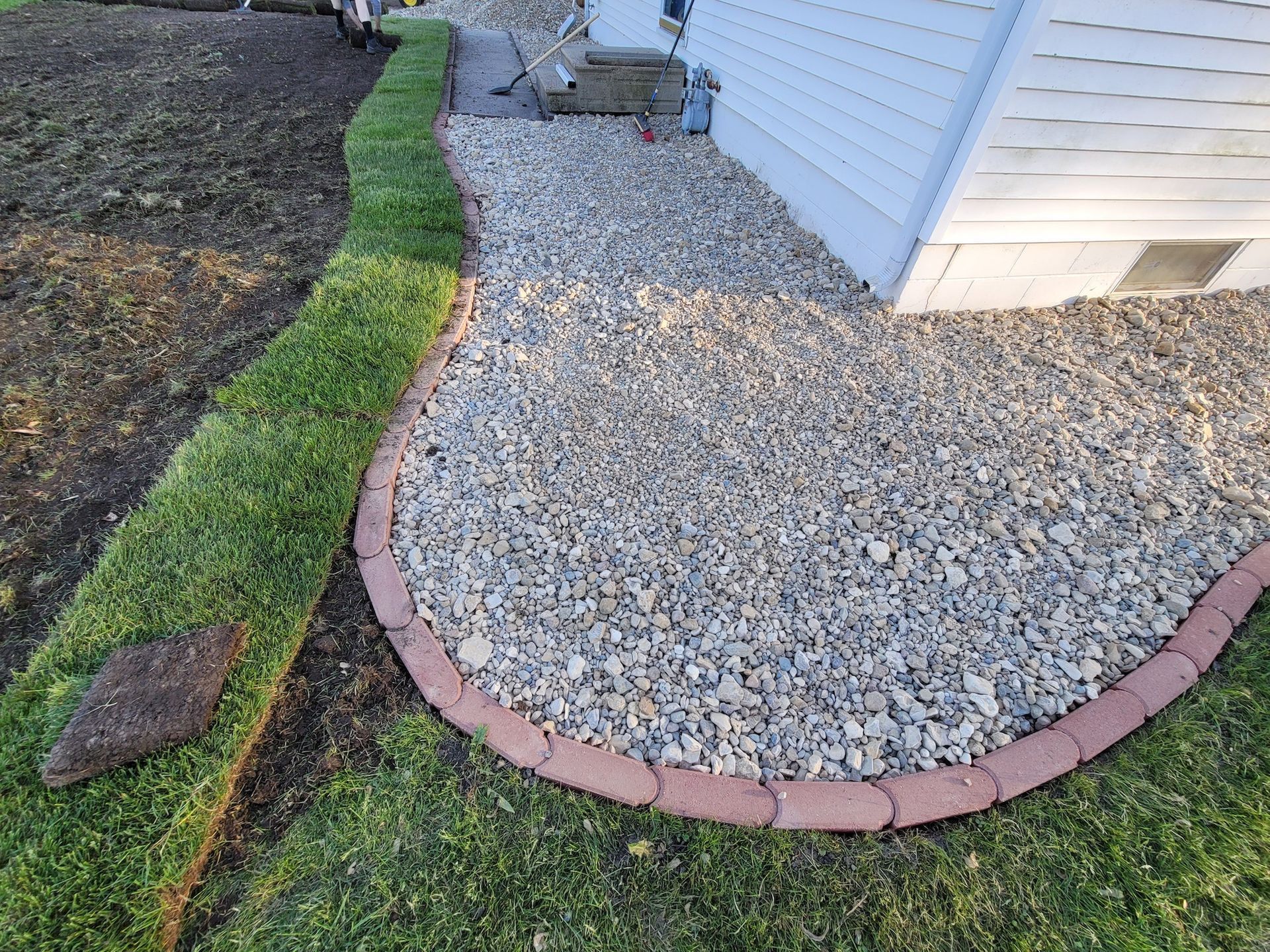 A sidewalk with a brick border and gravel in front of a house.