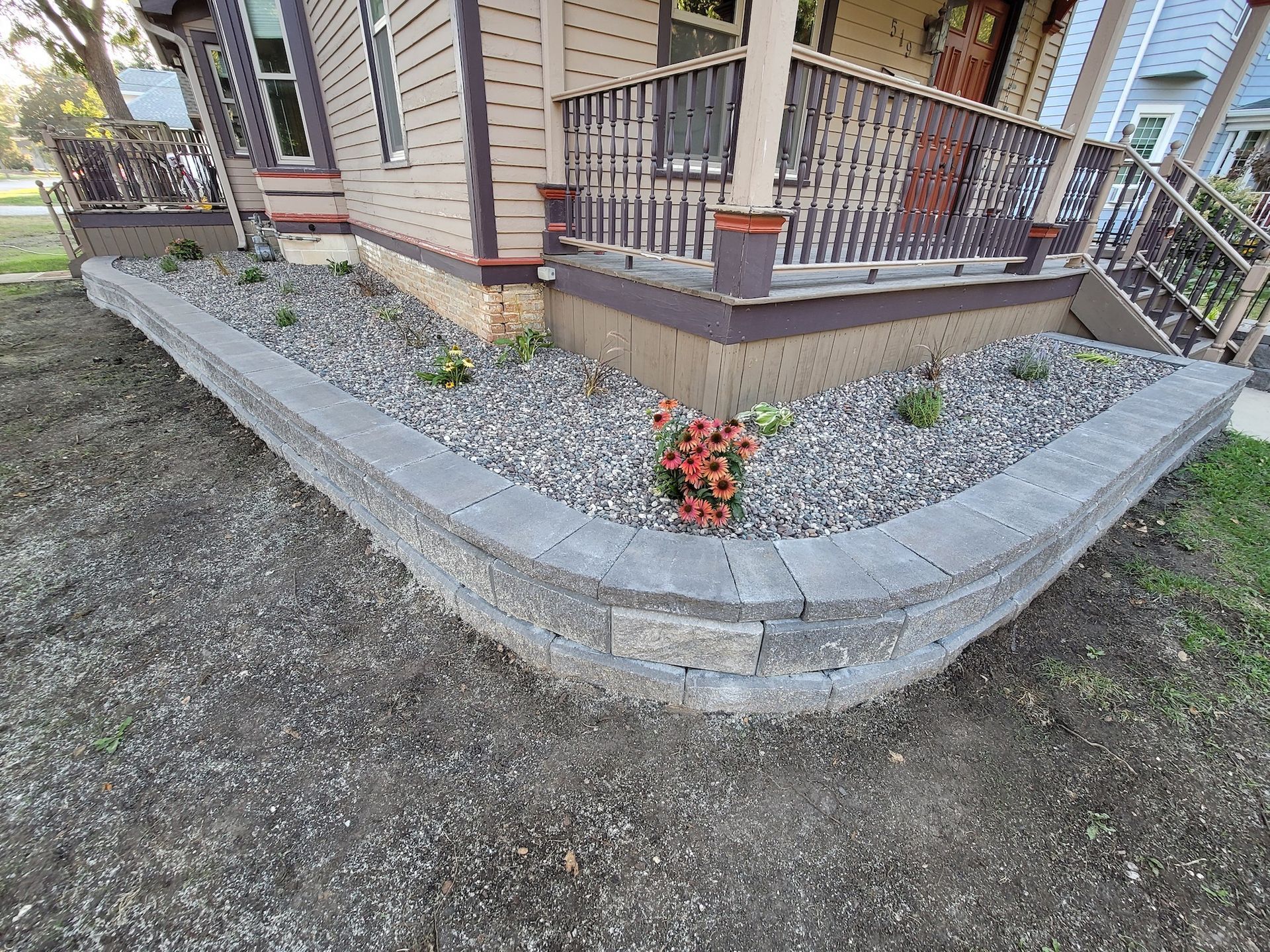A corner of a house with a planter and flowers in front of it.