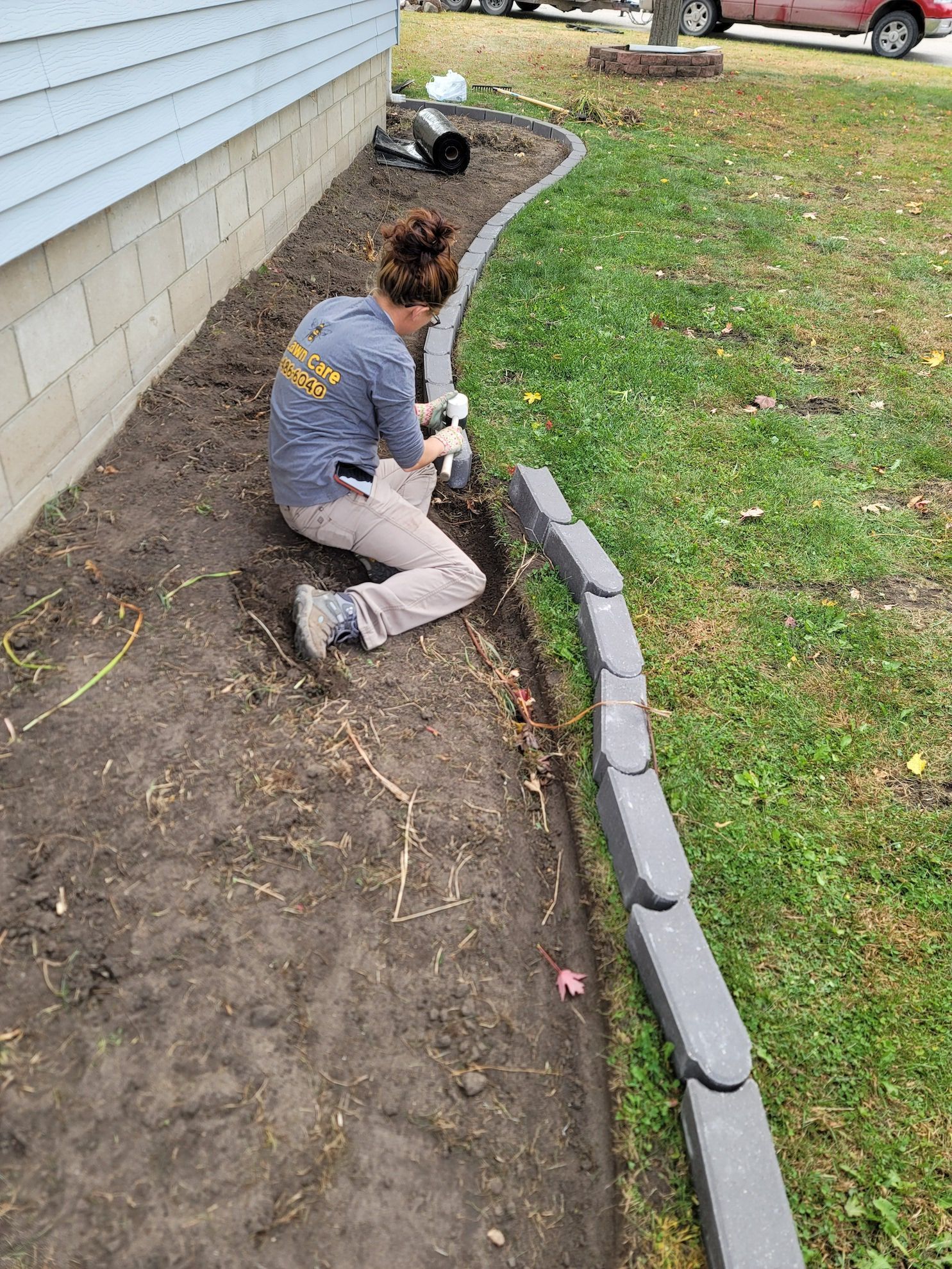 A woman is kneeling down in the dirt next to a house.