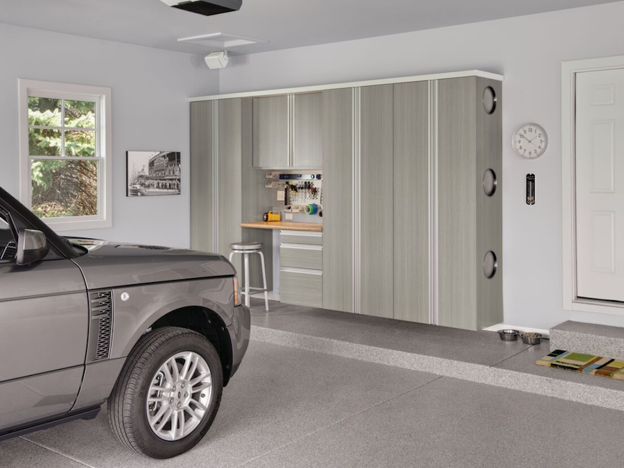 Stylish garage featuring custom cabinets, a workbench, and a luxury car parked inside.