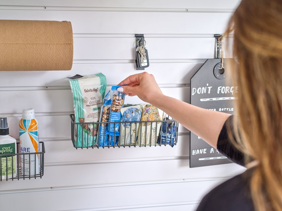 Close-up of a slatwall system with small baskets holding snacks, keys, and household items.