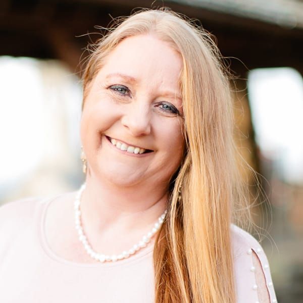 A woman with long blonde hair and a pearl necklace is smiling for the camera.