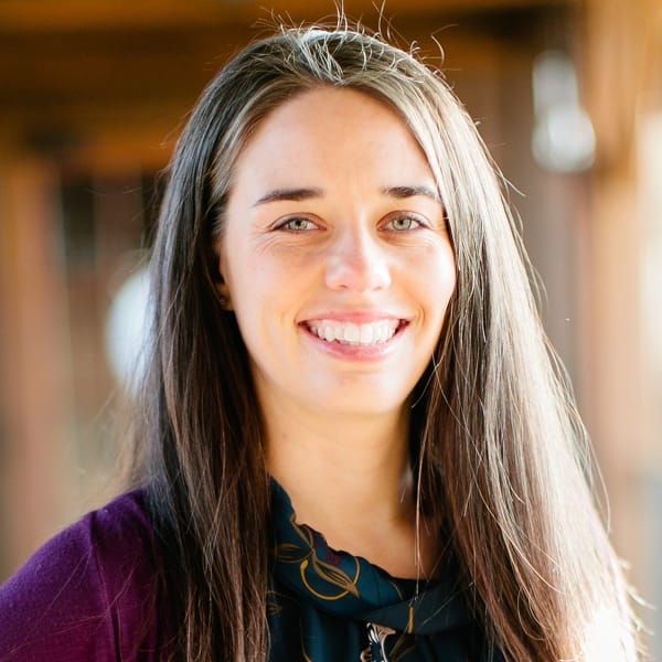 A woman with long hair is smiling and wearing a purple sweater.