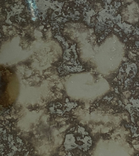 Close-up of a distressed mirror surface with mottled, brown and silver discoloration and light-colored patches.
