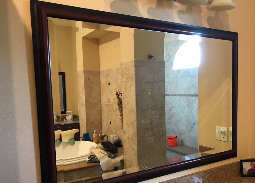 Large rectangular mirror reflecting a bathroom with a tub, shower, and sink. Dark brown frame, tan walls.