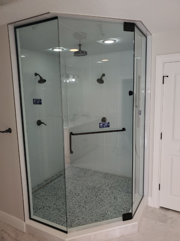 Pentagon-shaped glass shower with black framing, multiple showerheads, and a pebbled floor.