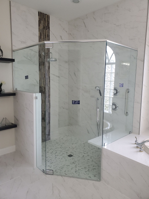 Glass shower enclosure with white marble tiles and mosaic shower floor.