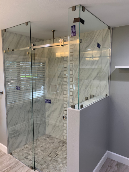 Glass shower enclosure with gray and white tile walls and gray walls.
