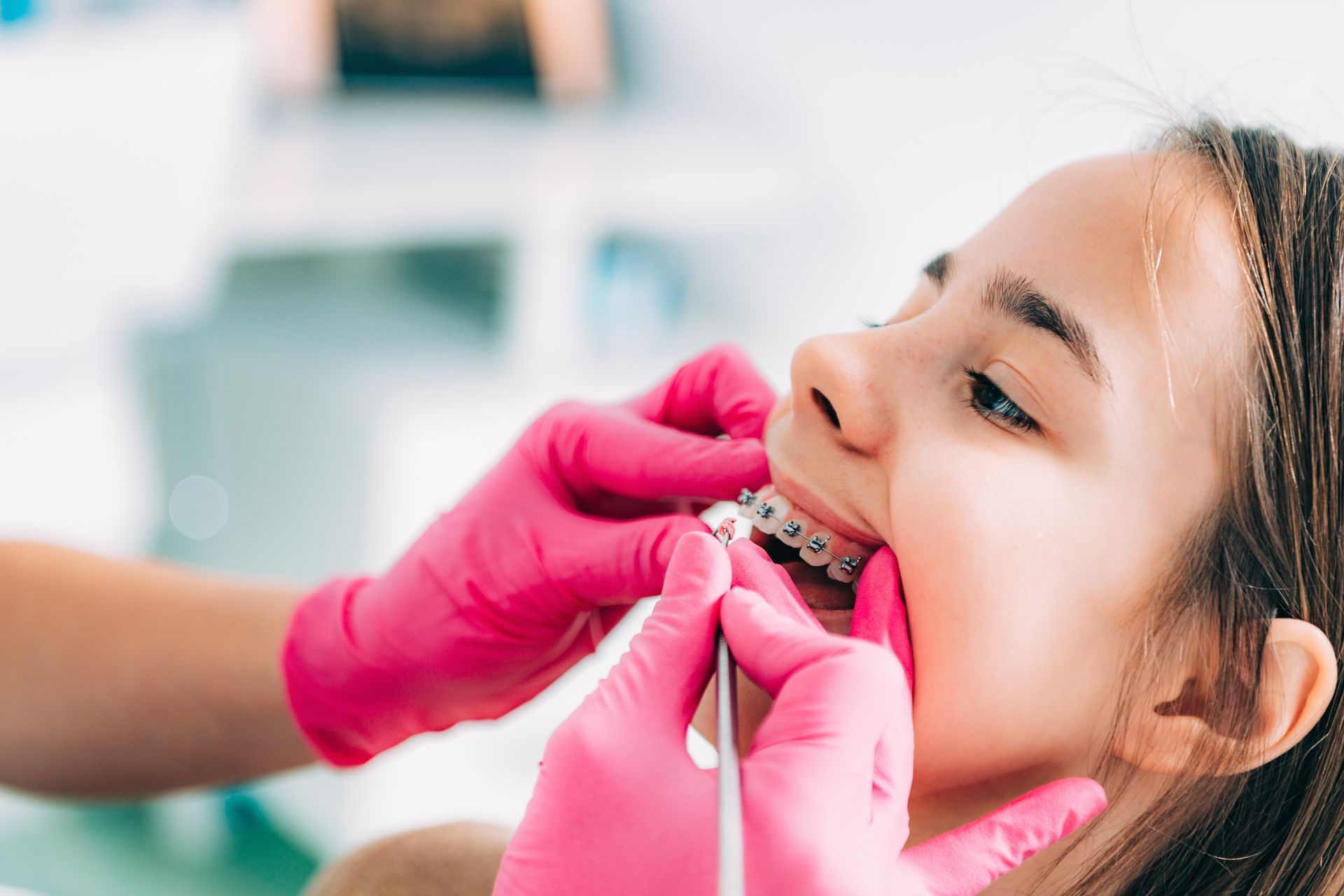 A dental professional wearing bright pink gloves adjusts braces on a patient’s teeth using a small metal tool.