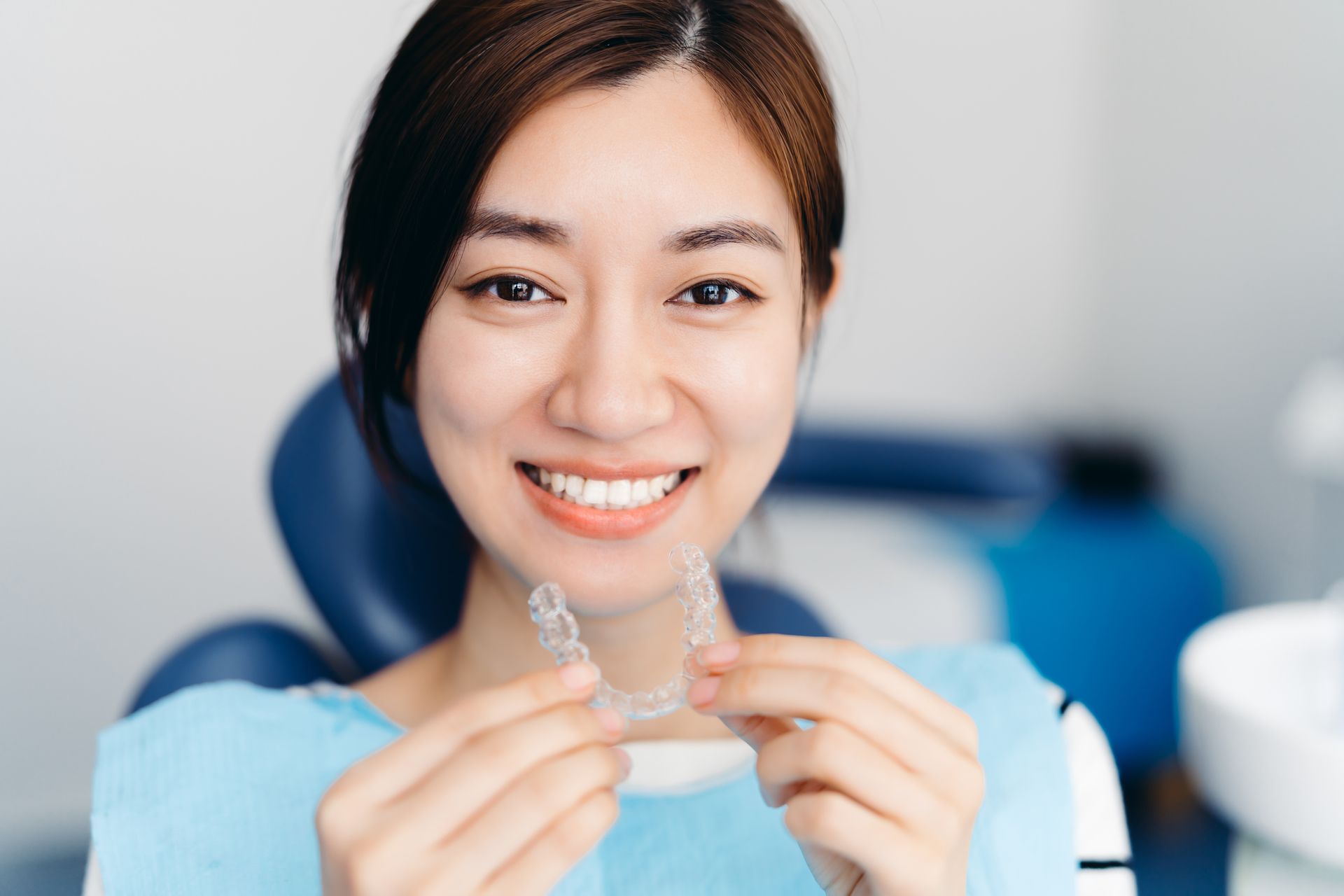 A woman is sitting in a dental chair holding a clear brace.