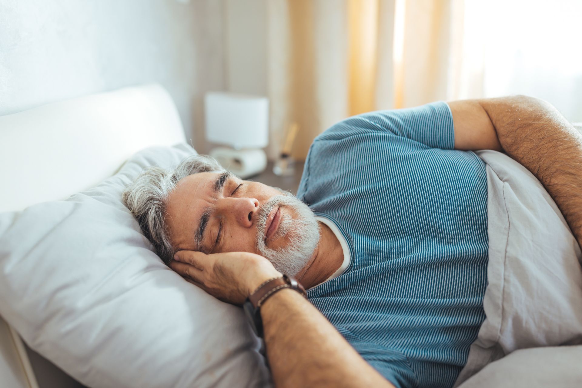 An older man is sleeping in a bed with his eyes closed. An older man is sleeping in a bed with his eyes closed.