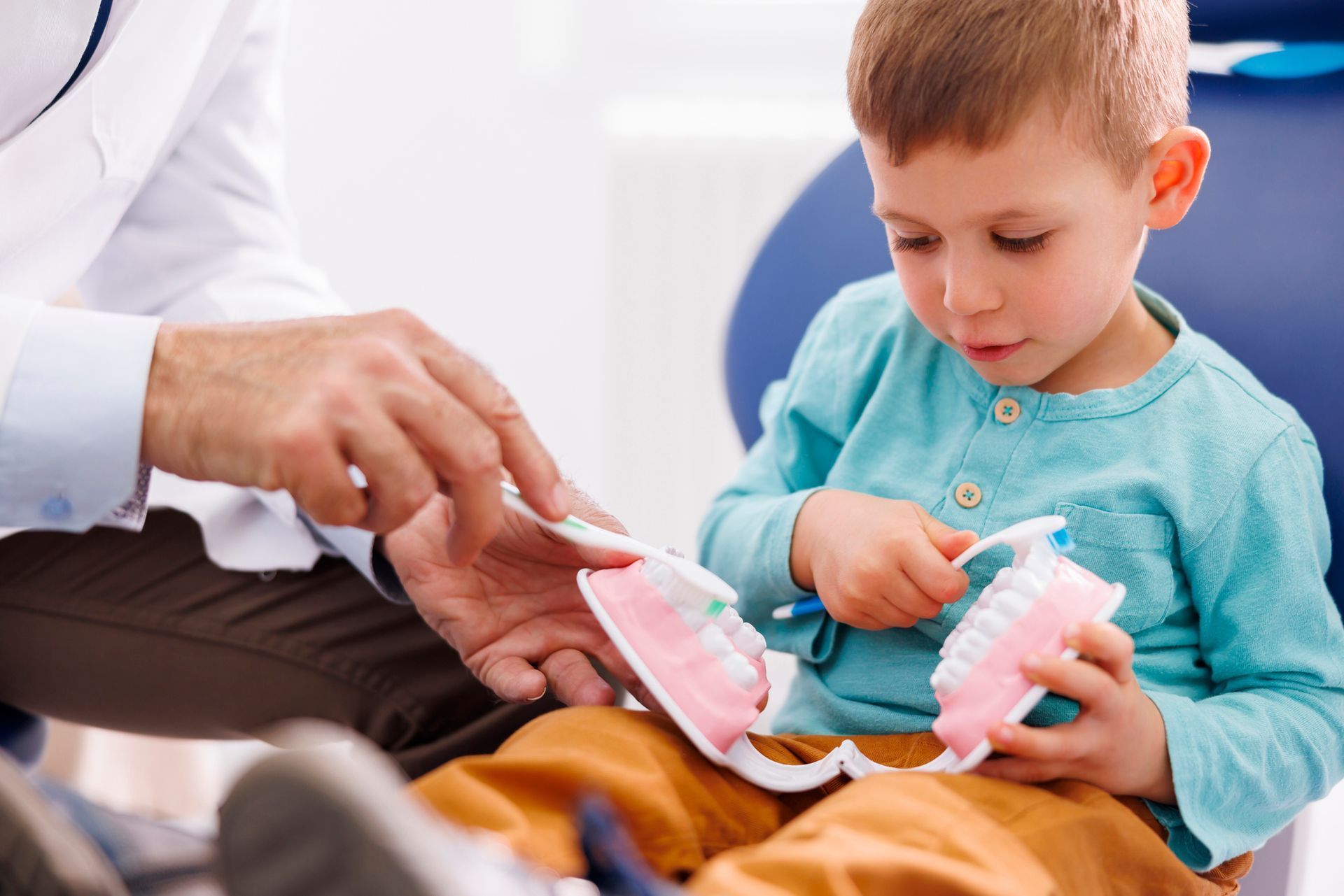 A dentist demonstrating teeth brushing to a little boy. A dentist demonstrating teeth brushing to a little boy.