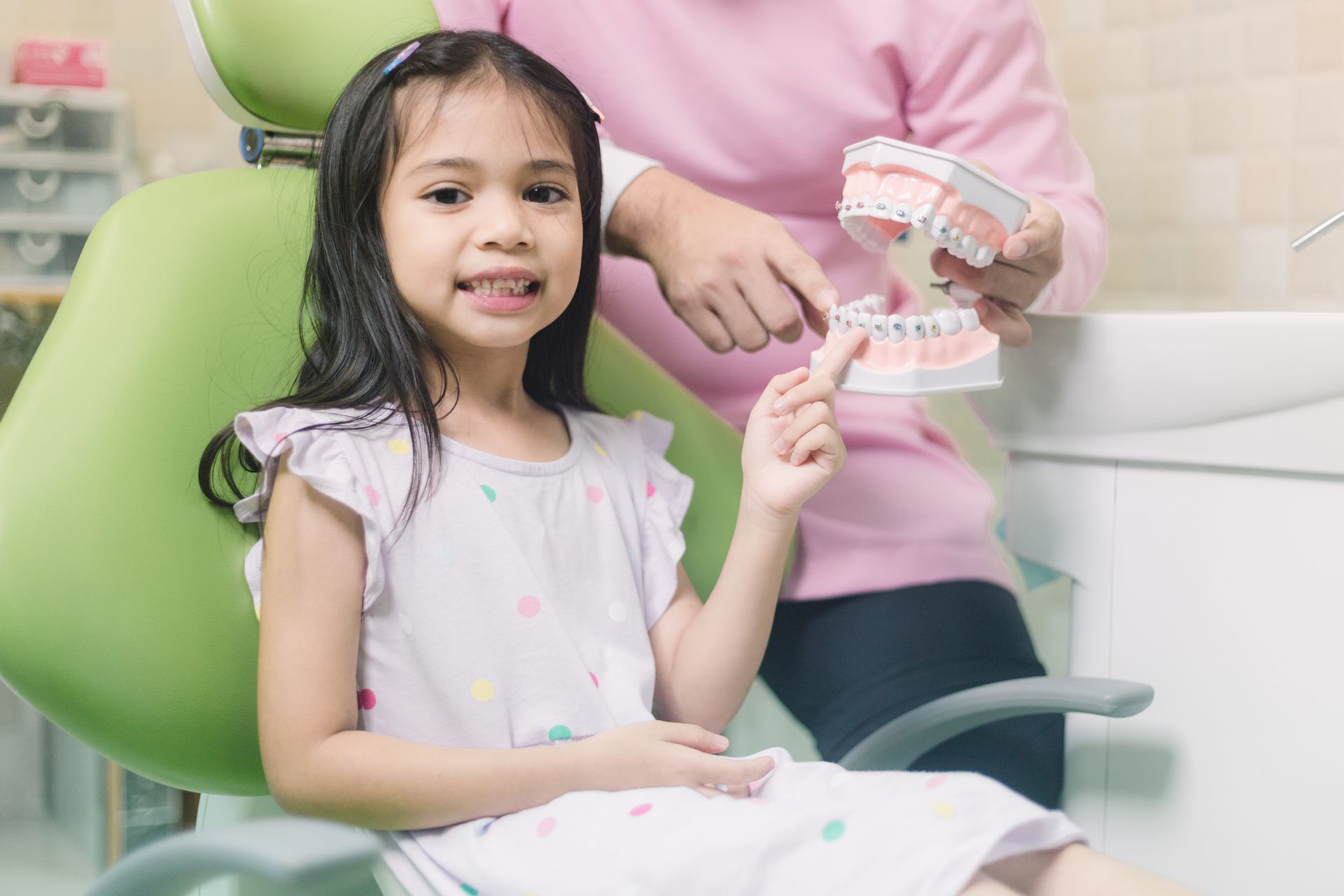 A little girl is sitting in a dental chair while a dentist shows her a model of teeth. A little girl is sitting in a dental chair while a dentist shows her a model of teeth.