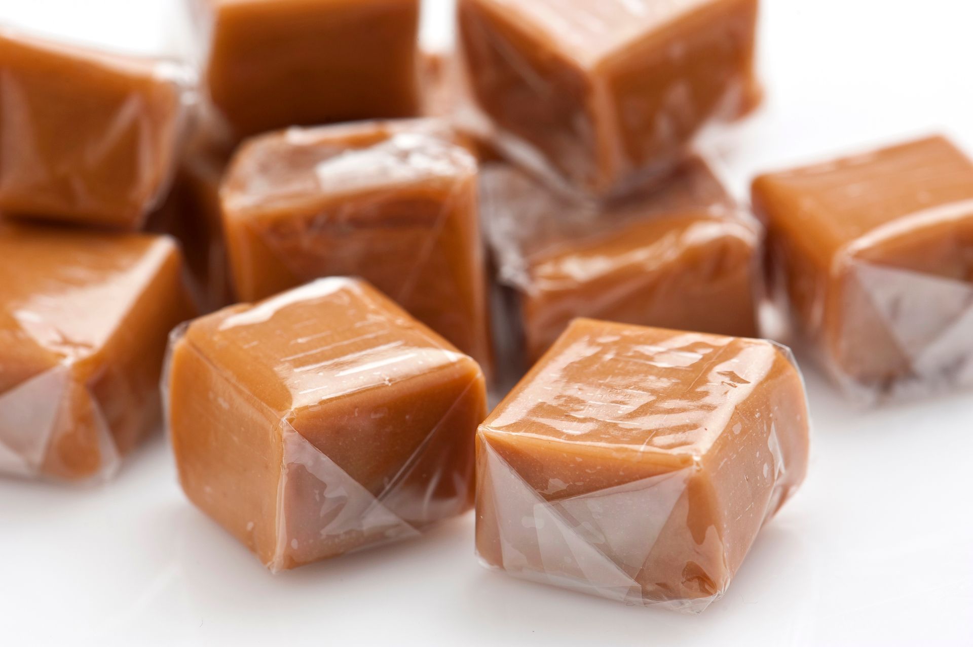 A pile of caramel candies wrapped in plastic on a white surface. A pile of caramel candies wrapped in plastic on a white surface.