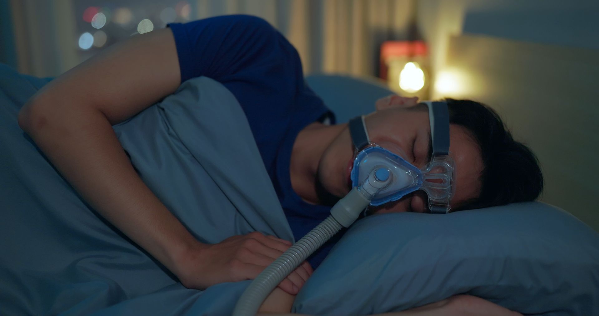 A man is sleeping in a bed with a cpap mask on his face. A man is sleeping in a bed with a cpap mask on his face.