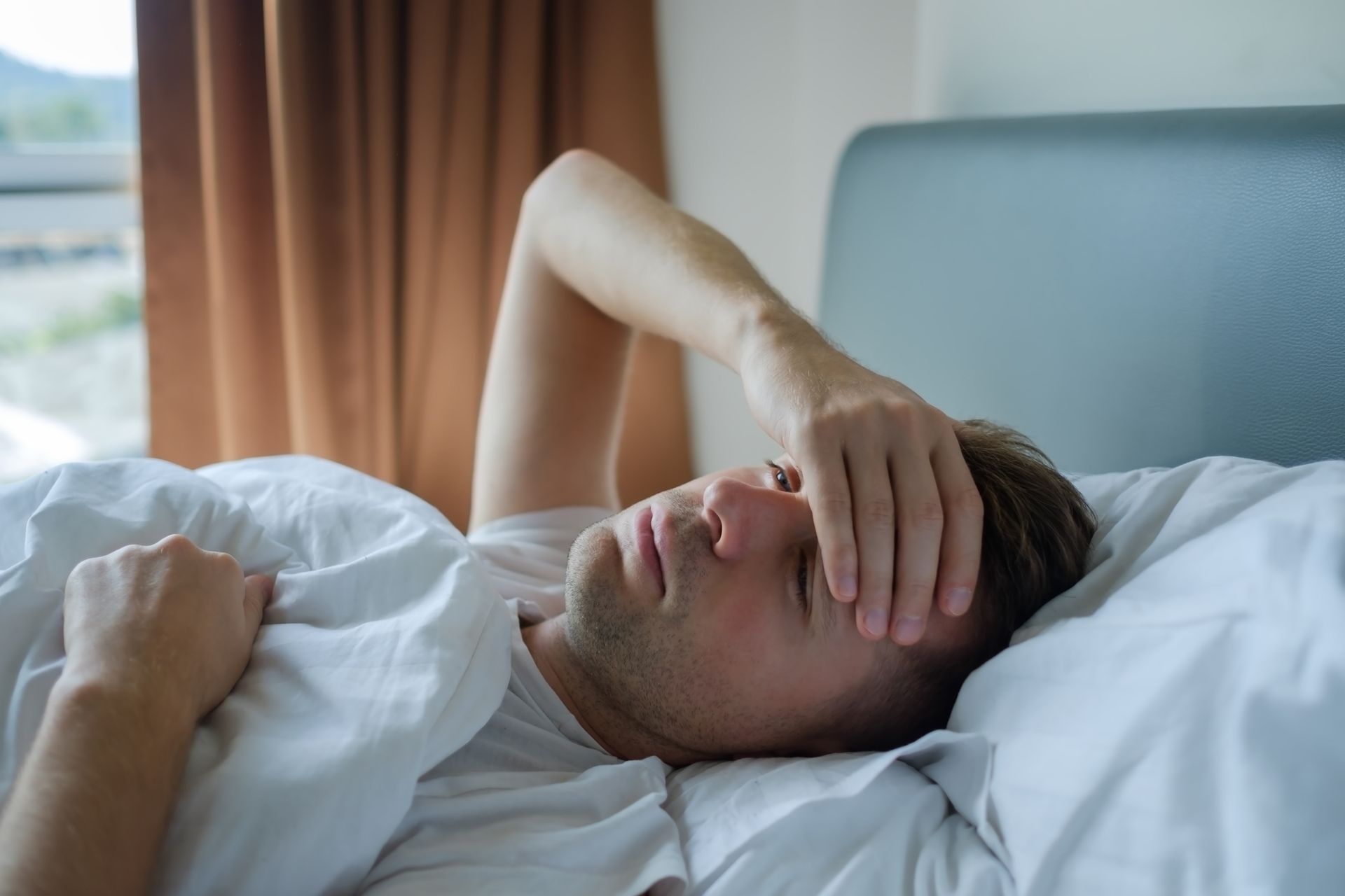 A man is laying in bed with his hand on his forehead. A man is laying in bed with his hand on his forehead.